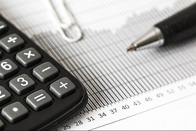 A Calculator, pin and pen placed on a paper