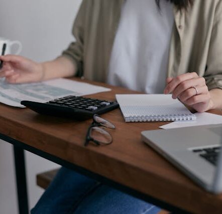 A lady filling forms on a desk with calculator and laptop besides her