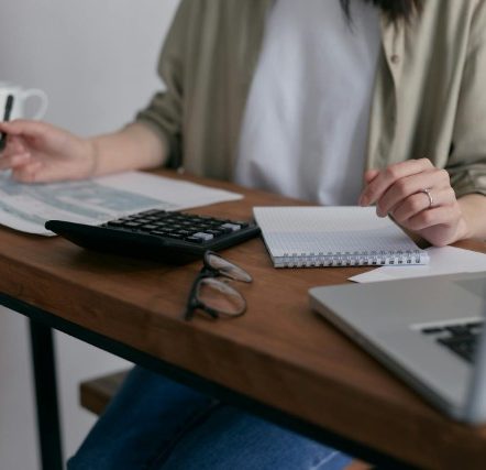 A female writing on paper on the table with laptop